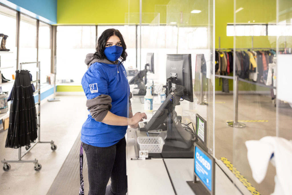 A person on the job, wearing a mask and standing behind one of the cashier terminals