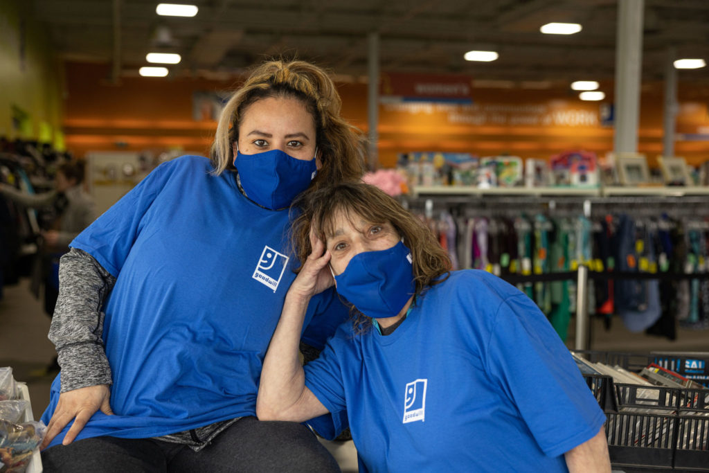 Two people working at Goodwill, wearing masks and posing for the camera