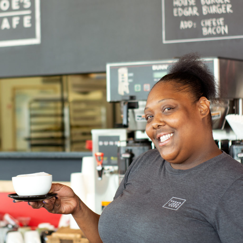 A barista smiles for the camera while showing a cup of coffee that she made