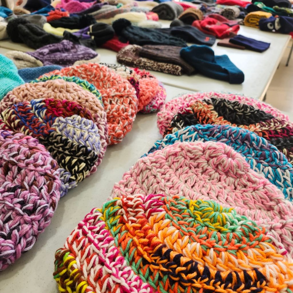 Knitted winter hats sit on a table at a donation drive.